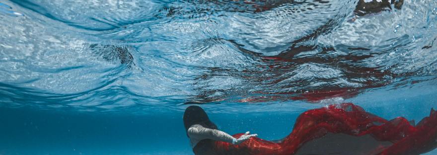 A mermaid with white skin and a red tail under blue water with waves crashing.